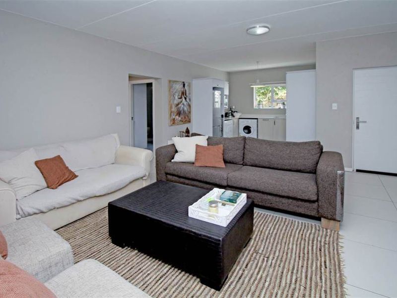 An open-plan living area featuring neutral tiled flooring, recessed lighting, and a seamless transition into the adjacent kitchen space.