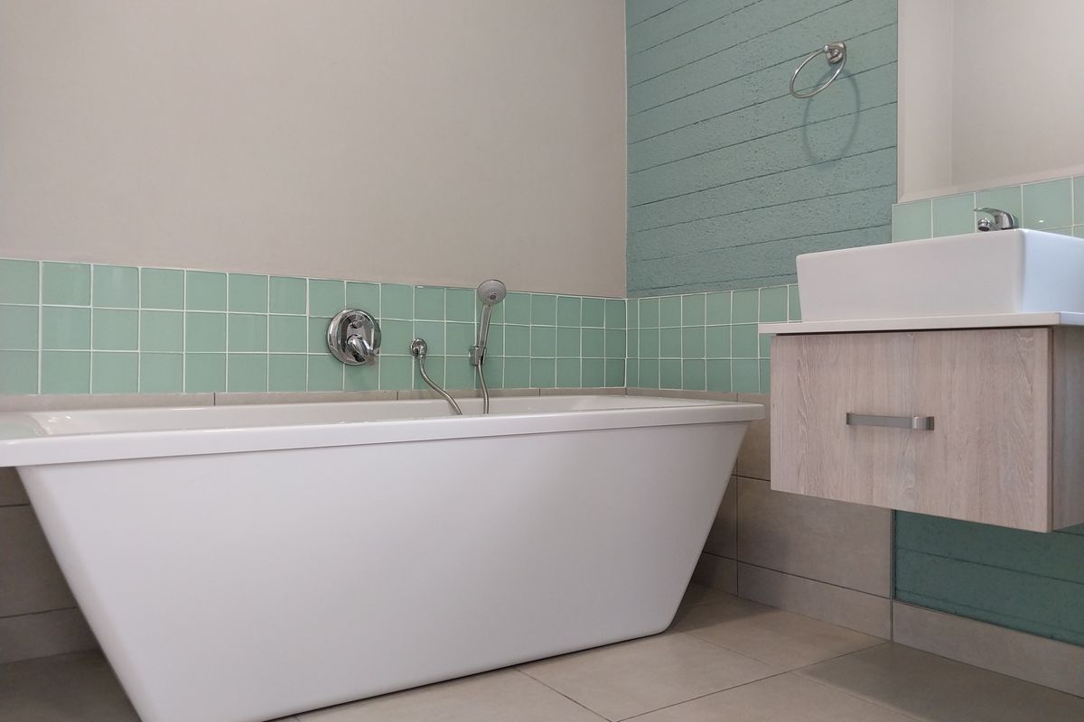 Modern bathroom featuring a sleek freestanding bathtub, floating vanity with a vessel sink, and stylish mint green tiled accents.