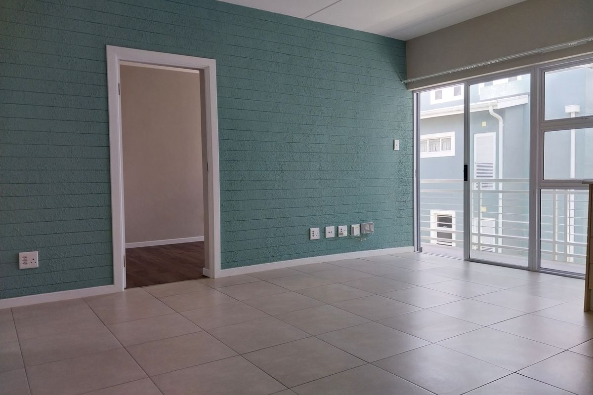 An empty living room featuring tiled flooring, a textured teal accent wall, and a sliding glass door providing access to a balcony.