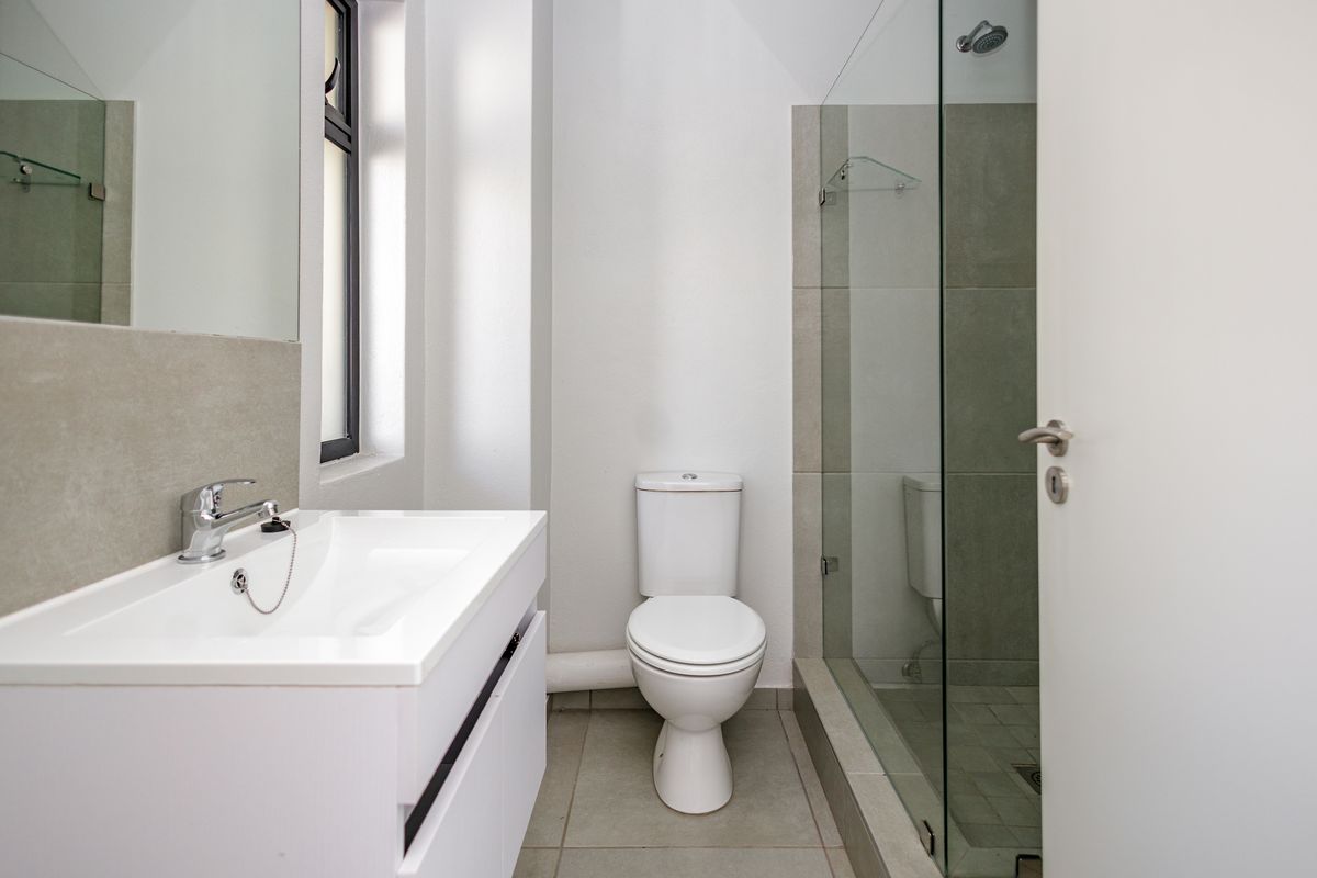 A modern, clean bathroom featuring a vanity with basin, a toilet, and a glass-enclosed shower with neutral tile finishes.