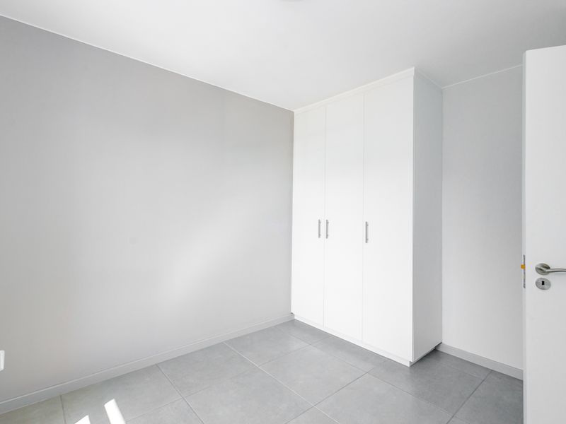 A clean, modern bedroom featuring neutral grey walls, large format floor tiles, and a white built-in wardrobe.