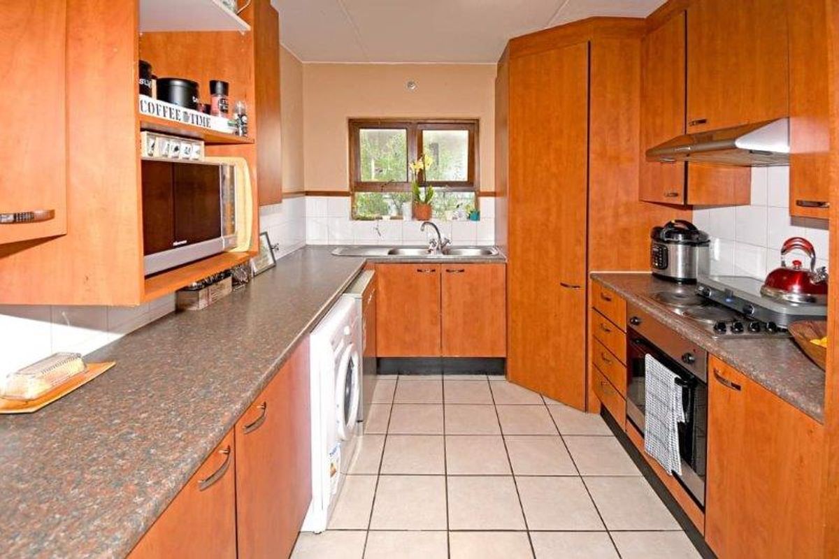 A functional kitchen featuring wood-finish cabinetry, laminate countertops, tiled flooring, a built-in oven, hob, and extractor fan with integrated laundry appliance space.