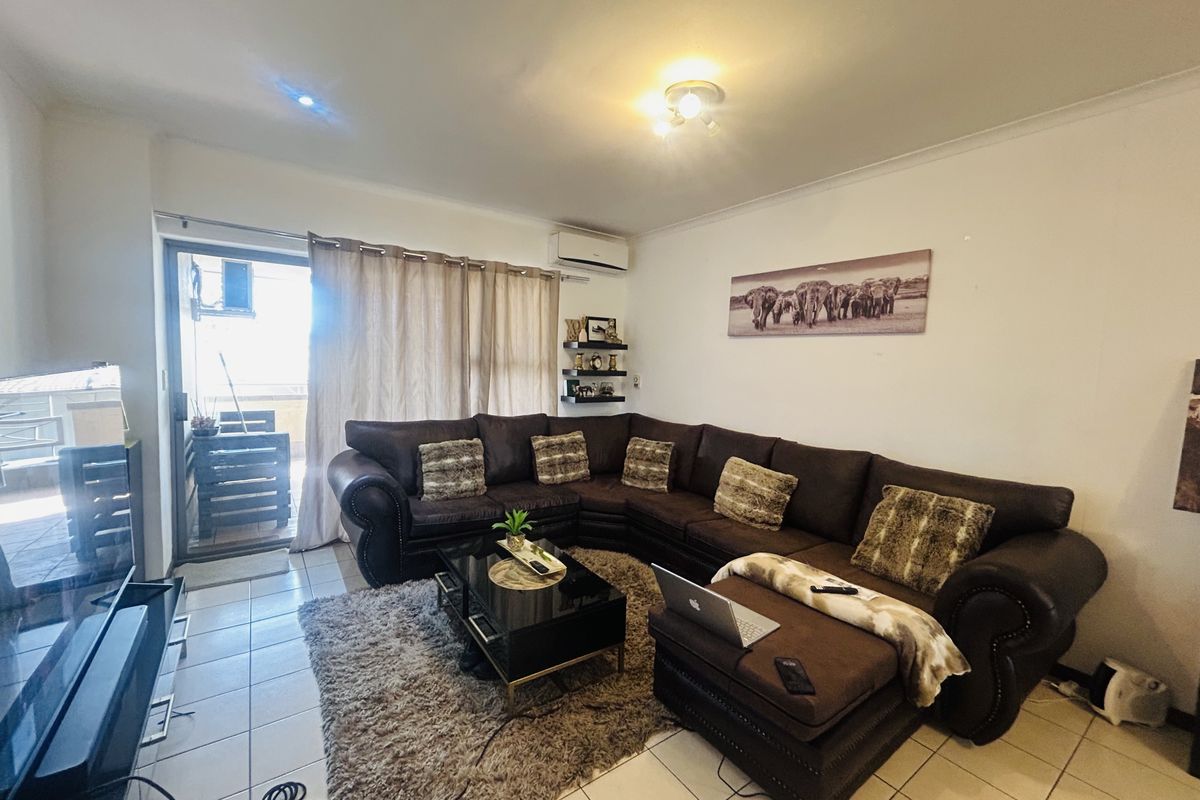A comfortable living room featuring tiled flooring, an air conditioning unit, and a sliding glass door providing access to an outdoor balcony area.