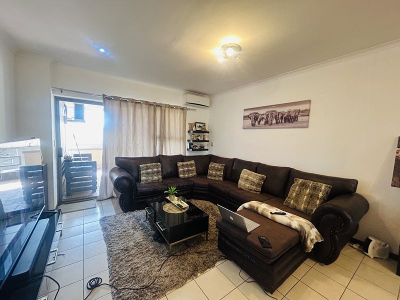 A comfortable living room featuring tiled flooring, an air conditioning unit, and a sliding glass door providing access to an outdoor balcony area.