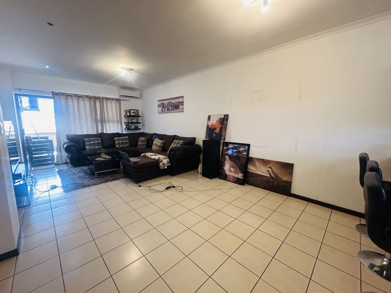 Spacious living area featuring tiled flooring, a wall-mounted air conditioning unit, and sliding door access to an outdoor balcony.