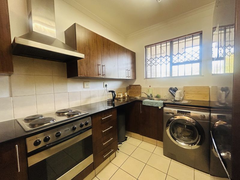 A functional kitchen featuring dark wood cabinetry, granite countertops, a built-in electric oven and stove, and a tiled backsplash with a window security gate.