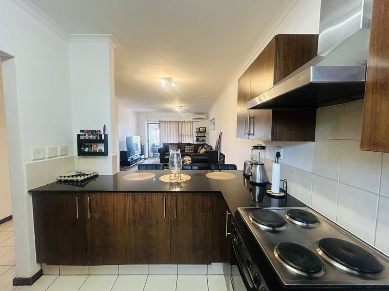 Open-plan kitchen featuring dark wood cabinetry, granite countertops, and an electric hob, flowing into a spacious living area.