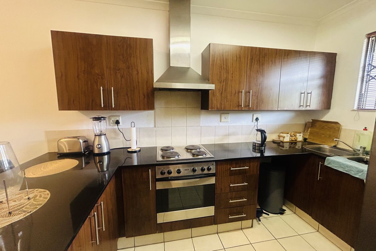 A functional kitchen featuring dark wood cabinetry, granite countertops, a stainless steel oven, hob, and extractor fan with tiled flooring and backsplash.