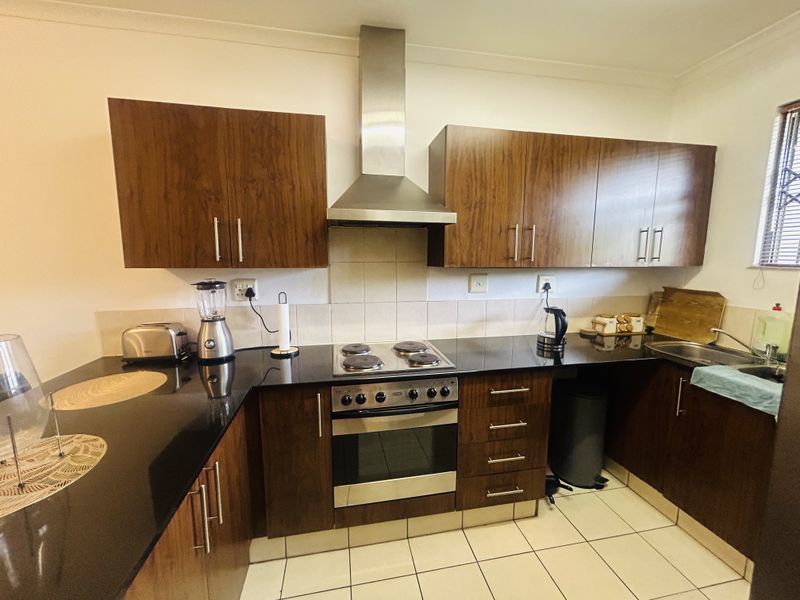 A functional kitchen featuring dark wood cabinetry, granite countertops, a stainless steel oven, hob, and extractor fan with tiled flooring and backsplash.