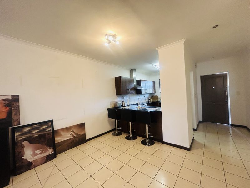 Open plan living area featuring tiled flooring and a functional kitchen with built-in cabinetry and a breakfast counter, leading to the main entrance.