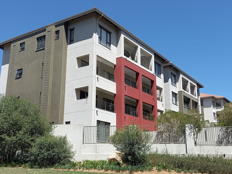 A view of the rear elevation of a multi-story cluster complex featuring balconies with metal railings and a secure perimeter wall.