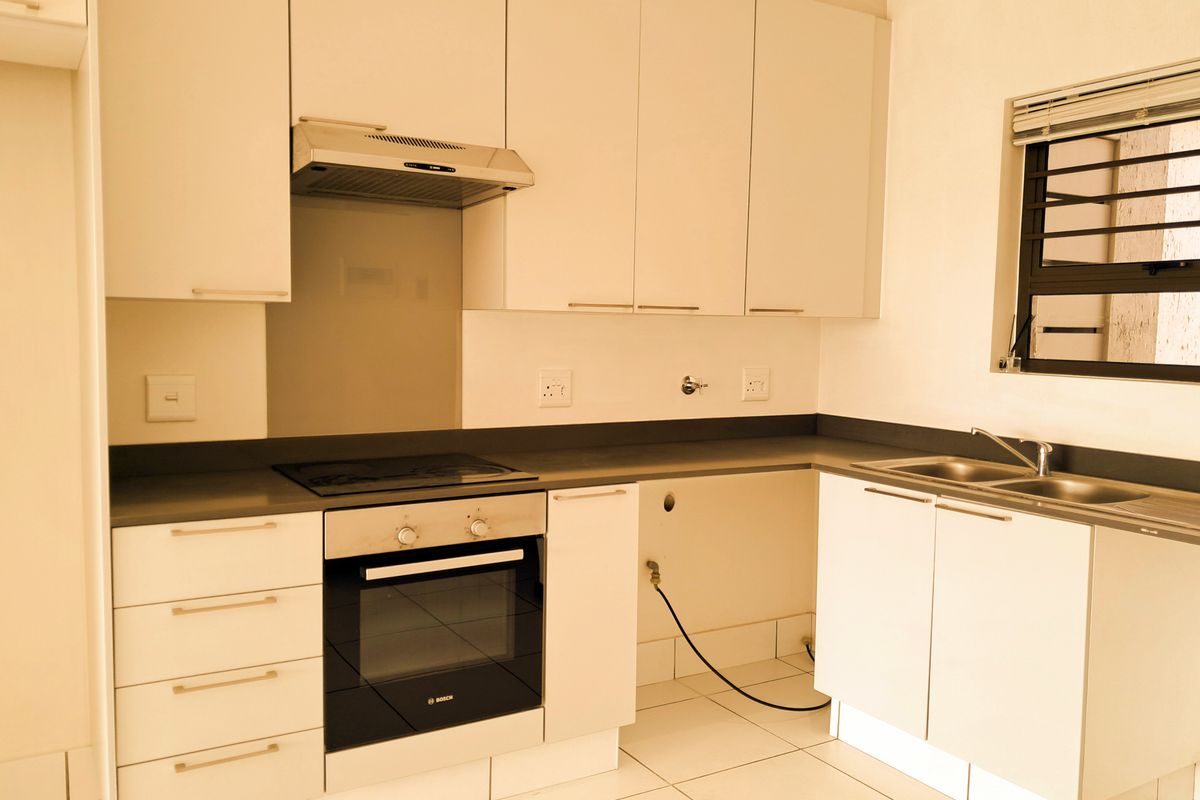 A clean, modern kitchen featuring white cabinetry, dark countertops, a built-in Bosch oven and hob, and tiled flooring.