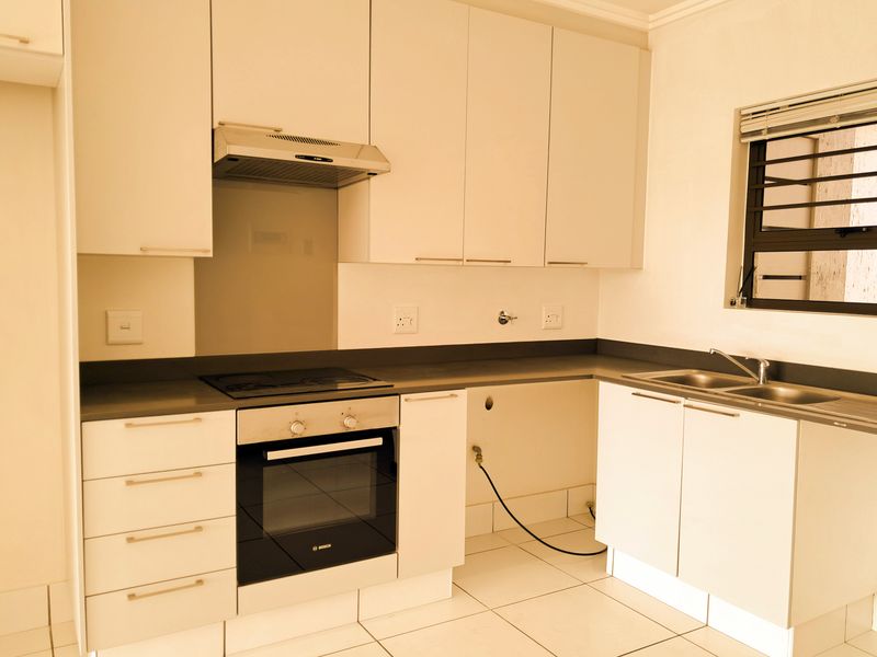 A clean, modern kitchen featuring white cabinetry, dark countertops, a built-in Bosch oven and hob, and tiled flooring.