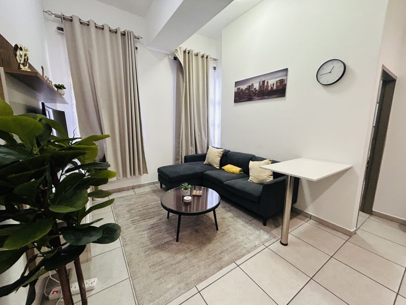 A well-maintained living room featuring ceramic floor tiles, high ceilings, and a wall-mounted breakfast bar, offering a functional and bright living space.