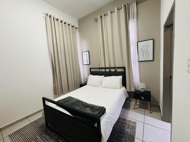 A well-maintained bedroom featuring neutral wall tones, tiled flooring, and dual window treatments, providing a clean and functional living space.