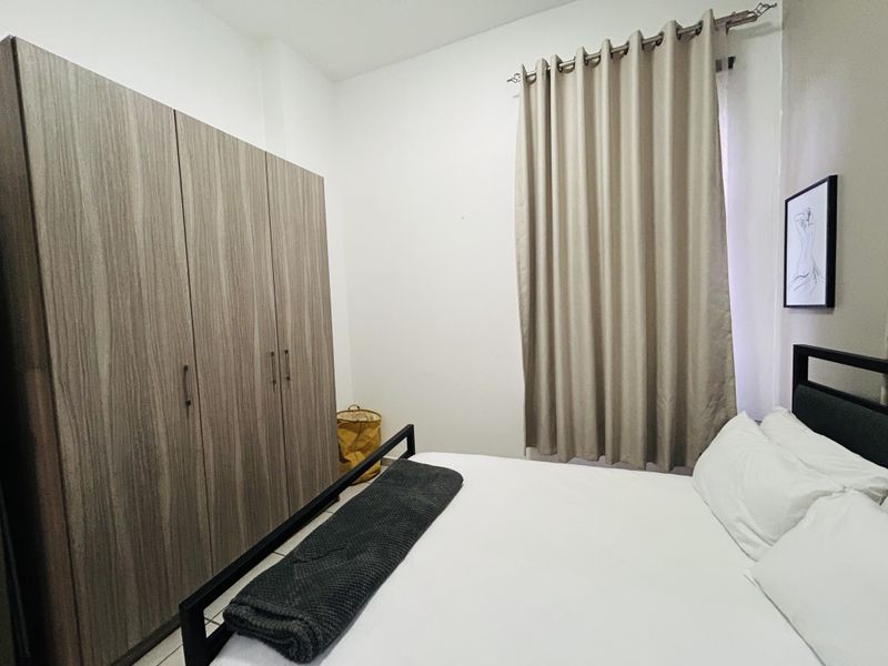 A well-maintained bedroom featuring a large built-in wardrobe with wood-grain finish and neutral curtains.