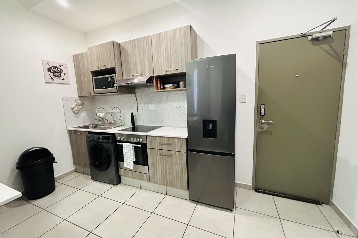 Compact modern kitchen featuring wood-grain cabinetry, integrated appliances, tiled backsplash, and ceramic flooring, conveniently located near the apartment entrance.