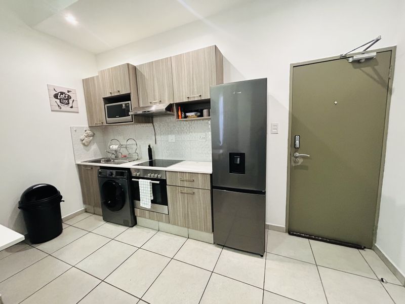 Compact modern kitchen featuring wood-grain cabinetry, integrated appliances, tiled backsplash, and ceramic flooring, conveniently located near the apartment entrance.