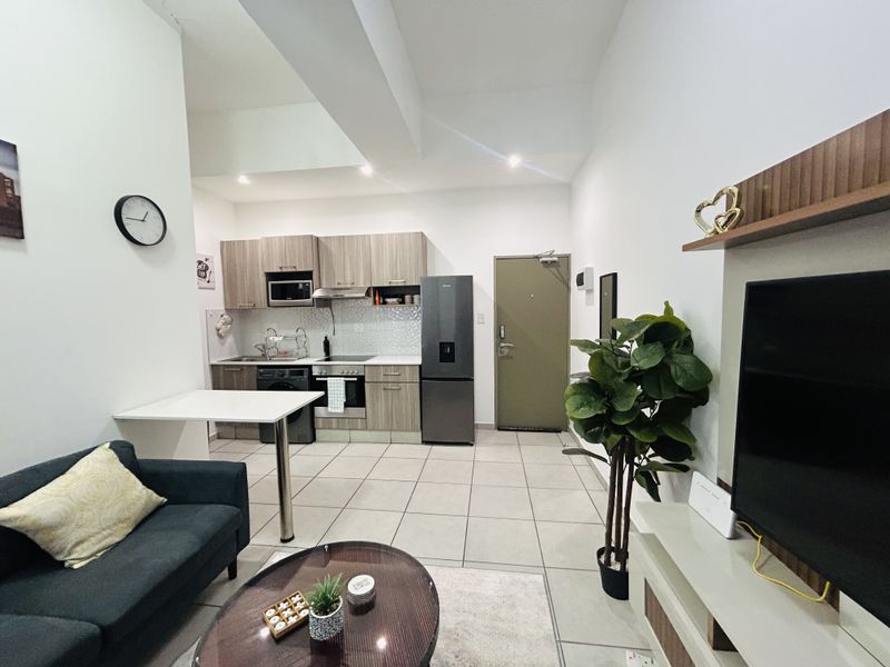 Modern open-plan apartment featuring a compact kitchen with built-in cabinetry and appliances, seamlessly flowing into the living area with tiled flooring throughout.