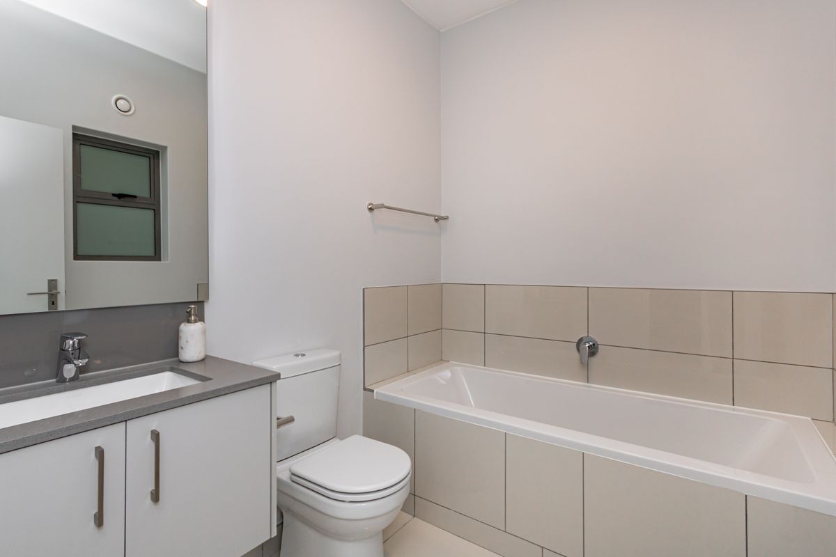 A clean, modern bathroom featuring a vanity with basin, a toilet, and a tiled bathtub area with wall-mounted fixtures.