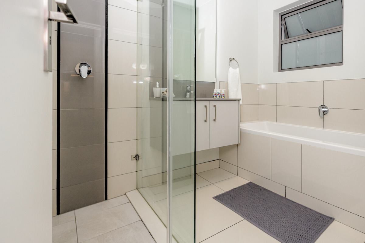 Modern bathroom featuring a glass shower enclosure, wall-mounted vanity, and a built-in bathtub with neutral tiled finishes.