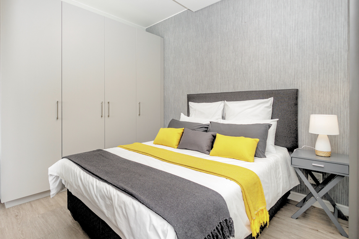 A well-maintained bedroom featuring floor-to-ceiling built-in cupboards, textured feature wallpaper, and light-toned laminate flooring.
