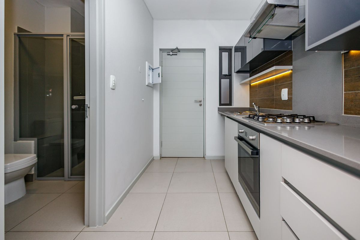 Modern kitchen featuring stone countertops, gas hob, built-in oven, and sleek cabinetry, with an adjacent bathroom visible through the doorway.