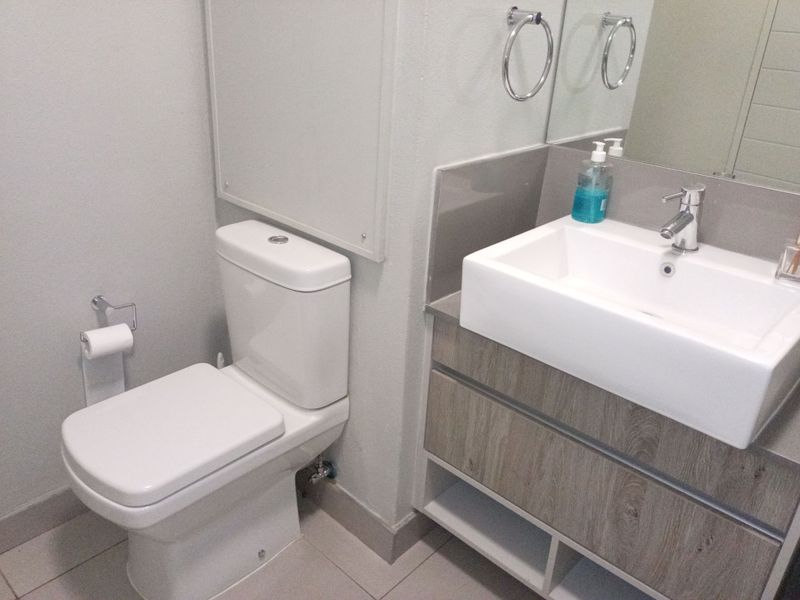 A modern bathroom featuring a wood-finish vanity with a vessel sink, chrome fixtures, and a clean, neutral tiled floor.