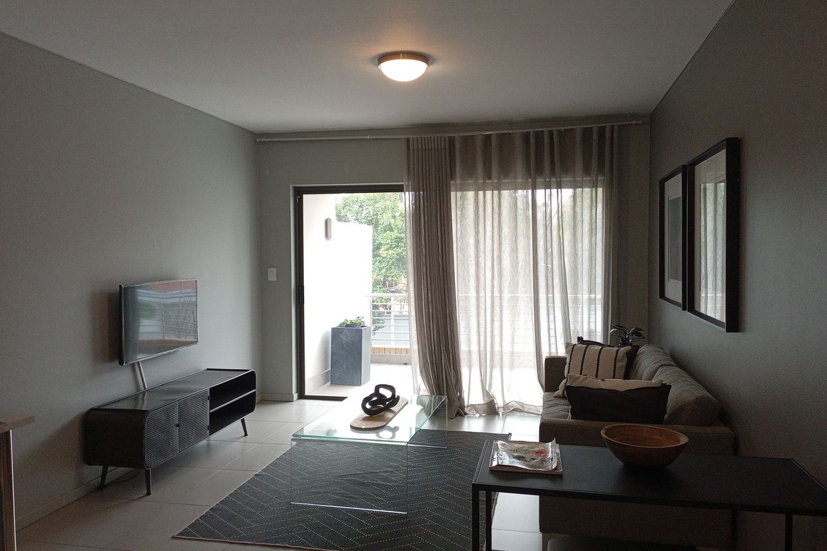 A well-maintained living room featuring neutral wall tones, tiled flooring, and a sliding glass door providing access to an outdoor balcony area.