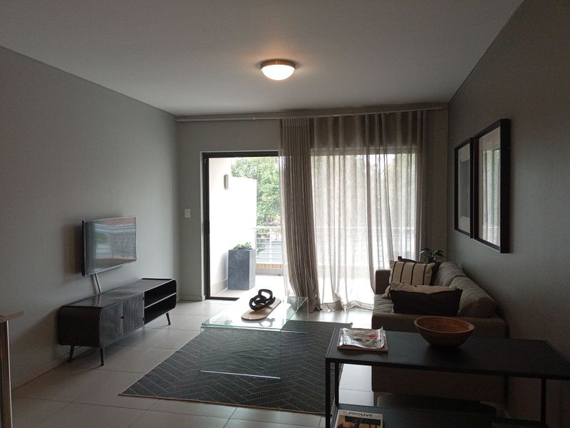 A well-maintained living room featuring neutral wall tones, tiled flooring, and a sliding glass door providing access to an outdoor balcony area.