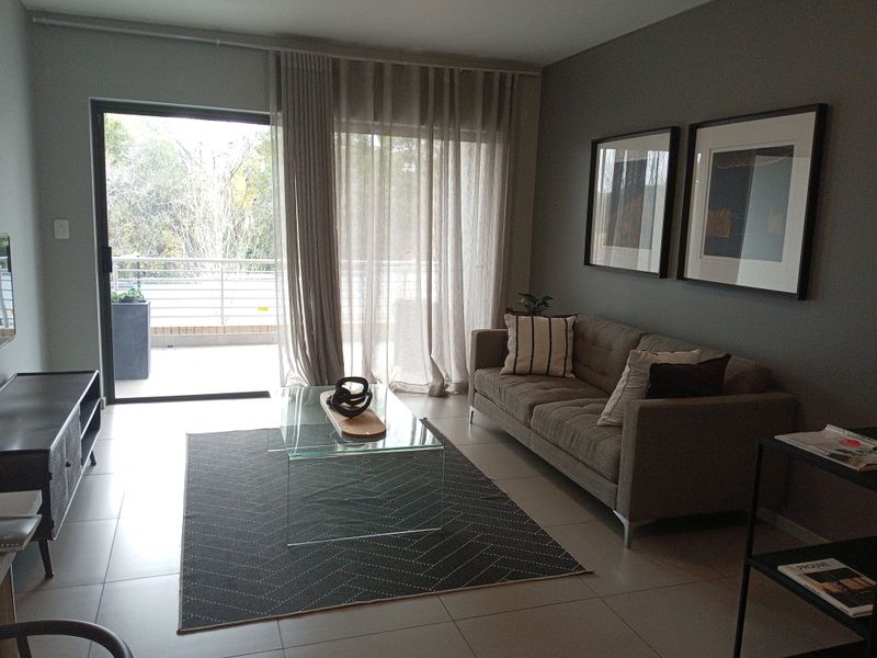 A well-maintained living room featuring large format floor tiles and a sliding glass door providing access to an outdoor balcony area.