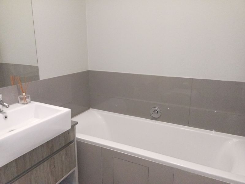 A modern bathroom featuring a built-in vanity with a basin, a bathtub with chrome fixtures, and neutral grey wall tiling.