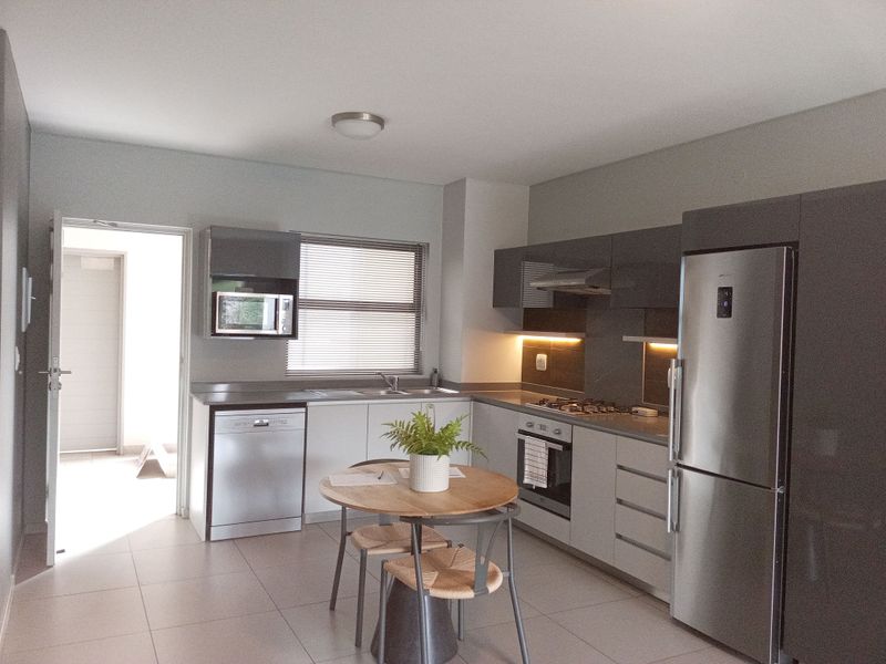 Modern kitchen featuring sleek grey cabinetry, stainless steel appliances, gas hob, integrated dishwasher, and tiled flooring with convenient access to an adjacent hallway.