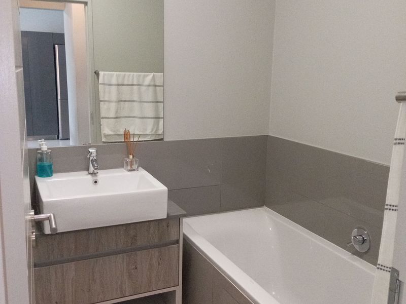 Modern bathroom featuring a wood-finish vanity with a vessel sink, a large wall mirror, and a clean bathtub with tiled splashback.