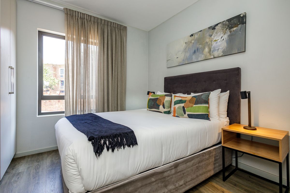 A well-maintained bedroom featuring modern wood-look flooring, built-in cabinetry, and a large window with neutral curtains, providing a bright and comfortable living space.