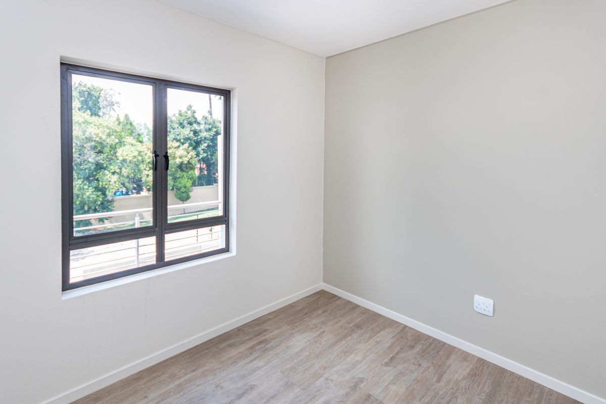 A bright, empty bedroom featuring modern wood-look flooring, neutral wall tones, and a large window providing natural light and exterior views.