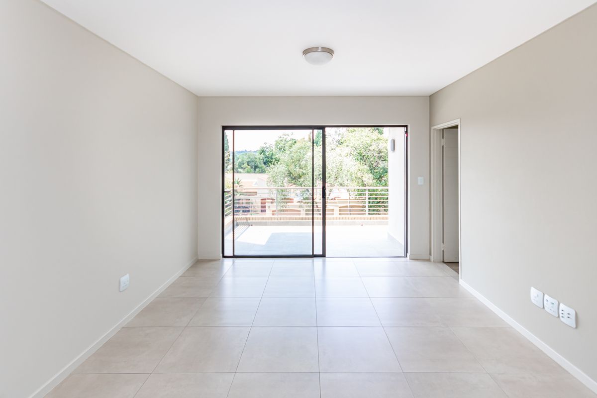 A bright, empty living area featuring neutral tiled flooring and large sliding glass doors that open onto a private balcony.