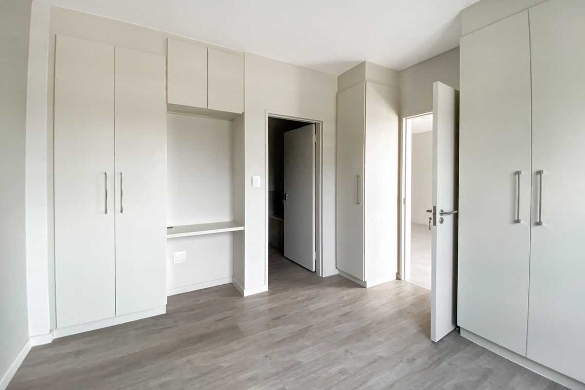 A bright bedroom featuring modern built-in cupboards, a dedicated desk nook, and light wood-look flooring.