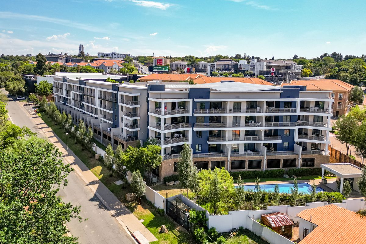Aerial view of a modern multi-story apartment complex featuring private balconies, a swimming pool, and landscaped grounds in a suburban setting.
