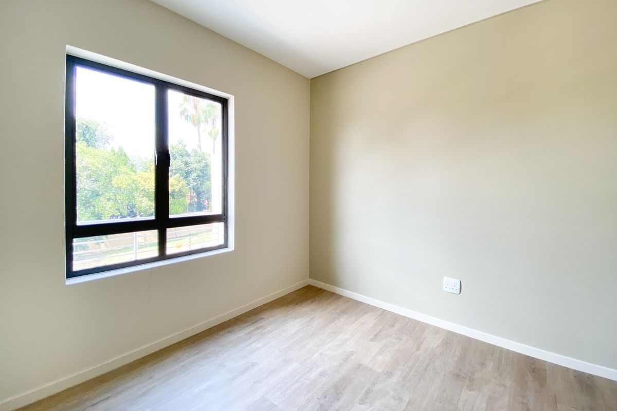 A bright, empty bedroom featuring neutral wall tones, modern wood-look flooring, and a large window providing natural light and exterior views.