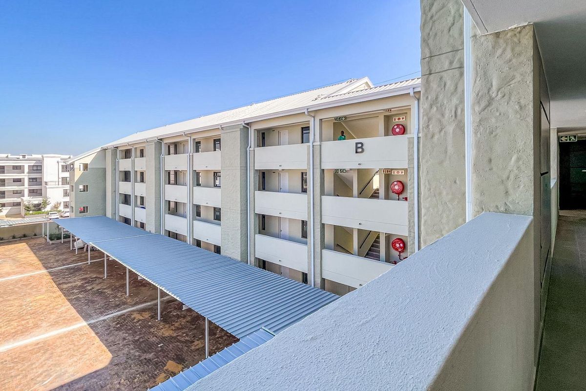 View of the apartment complex exterior, featuring covered parking bays, multi-story residential blocks, and external stairwell access.