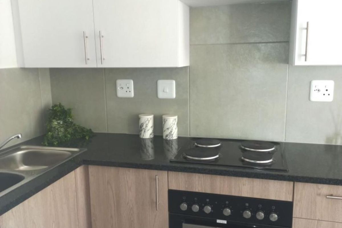 Modern kitchen featuring light wood-grain cabinetry, contrasting black granite countertops, a built-in oven, and a glass-top hob with a tiled splashback.