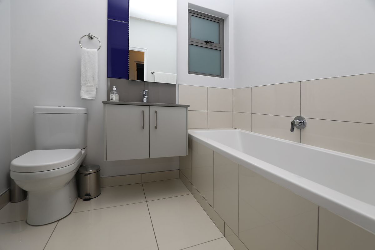 A modern, well-maintained bathroom featuring a bathtub, vanity cabinet with basin, toilet, and neutral tiled finishes.