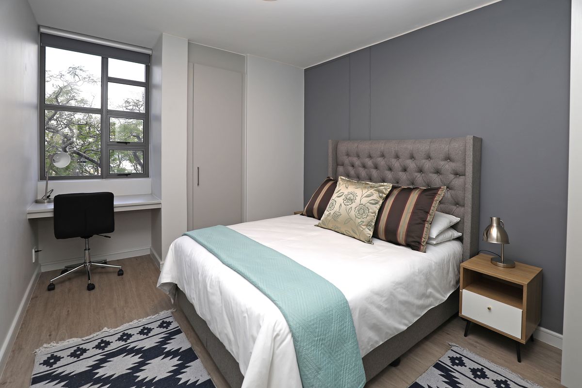 A well-maintained bedroom featuring laminate flooring, a built-in desk, and a built-in cupboard, complemented by a modern grey feature wall.