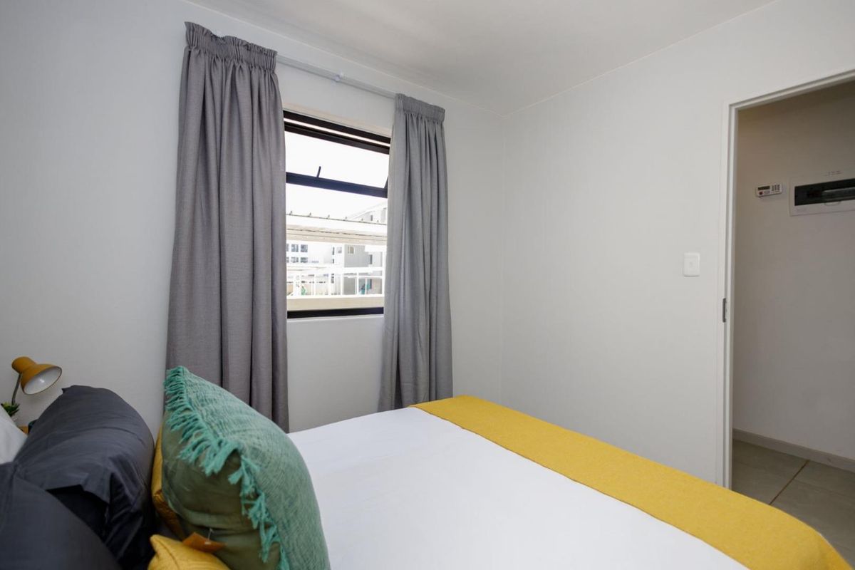 A bright bedroom featuring a window with curtains and a doorway leading to an adjacent space.