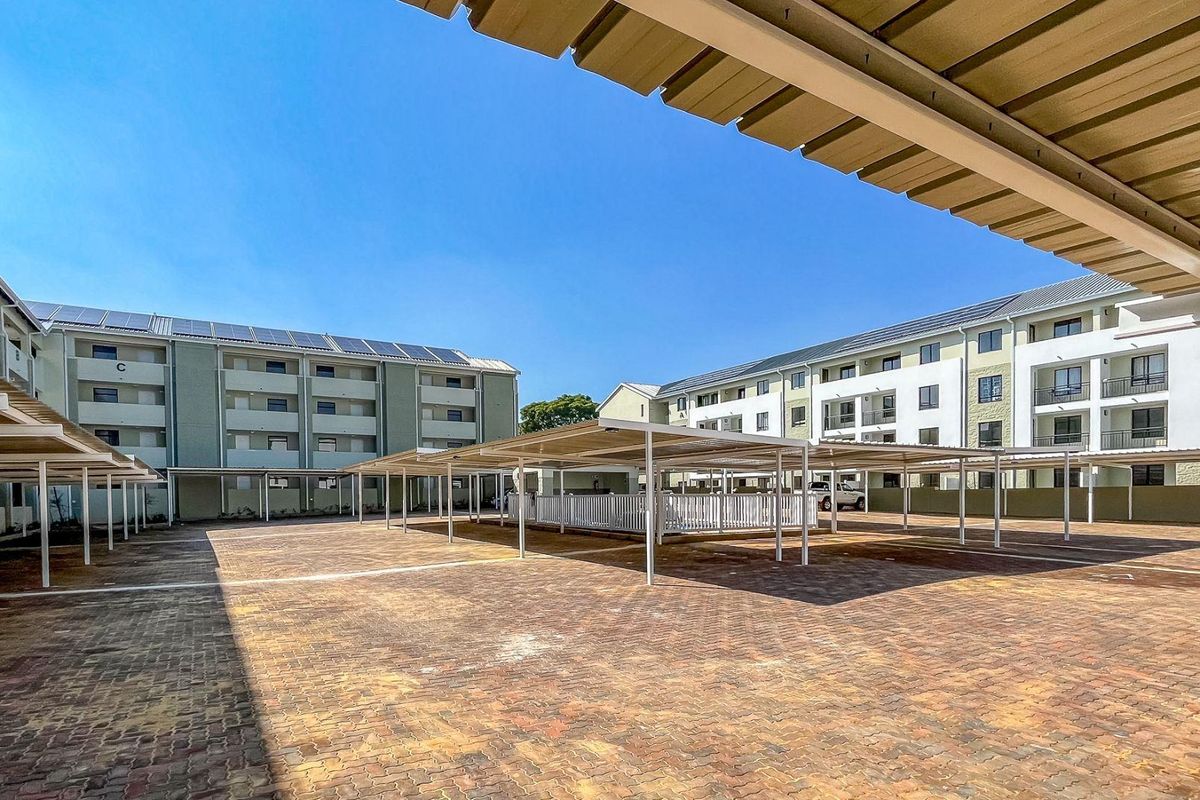 A view of the apartment complex parking area featuring covered parking bays and paved ground surfaces between the residential buildings.