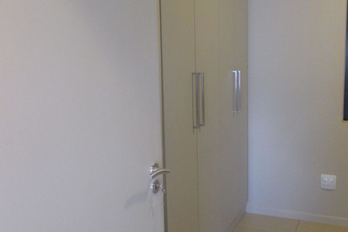 A clean, neutral bedroom featuring built-in cupboards and tiled flooring, offering a blank canvas for personalization.