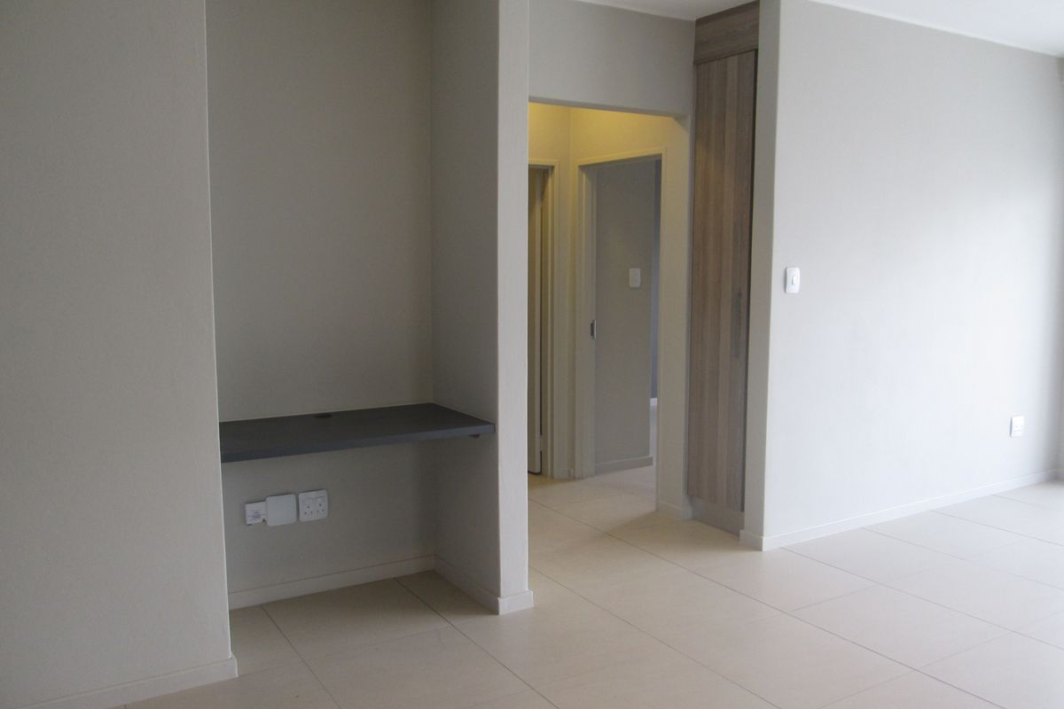 A bright, modern living area featuring neutral tiled flooring, a built-in desk nook, and a tall built-in storage cupboard.