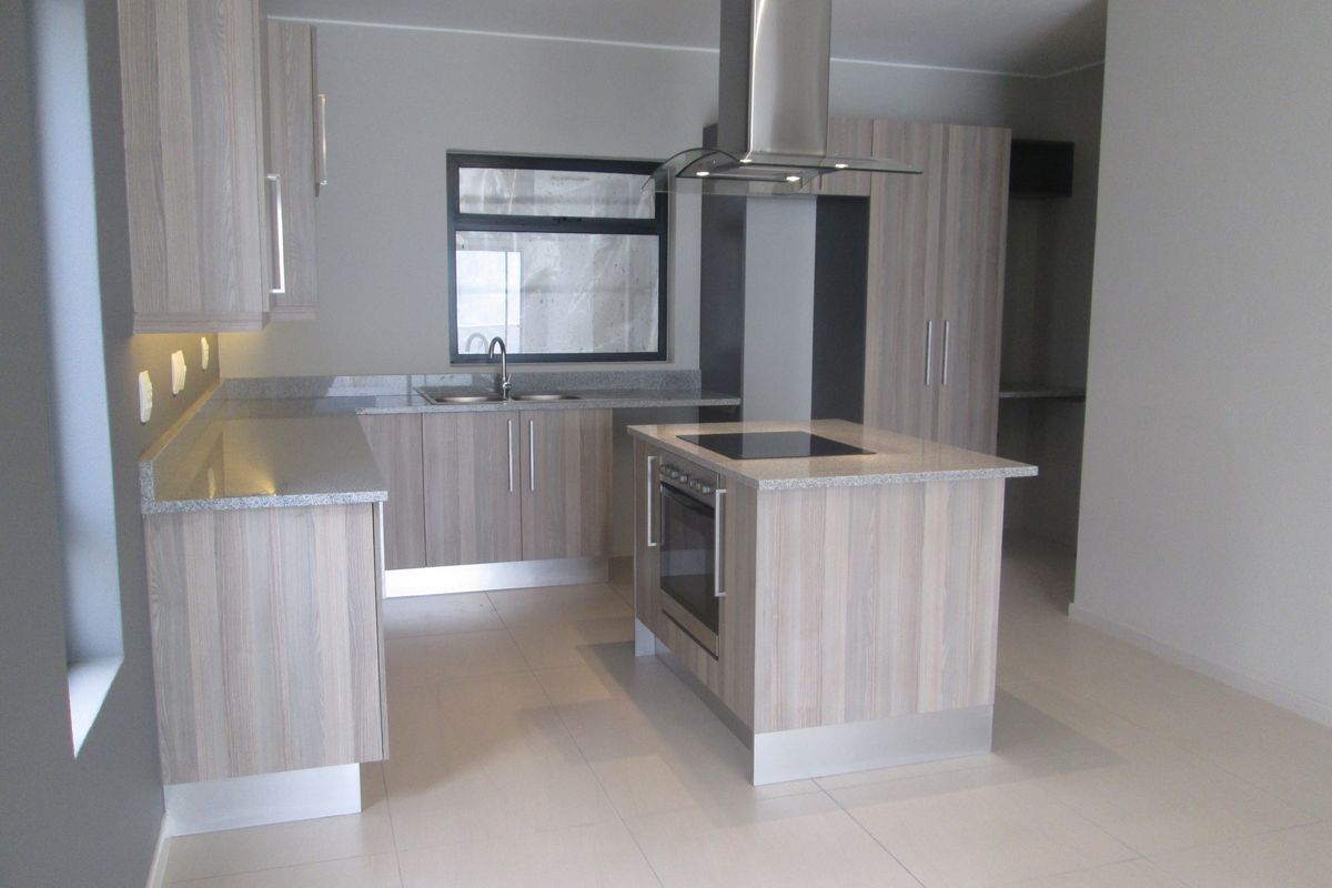 Modern kitchen featuring light wood-grain cabinetry, stone countertops, a central island with a built-in oven and cooktop, and sleek stainless steel extractor fan.