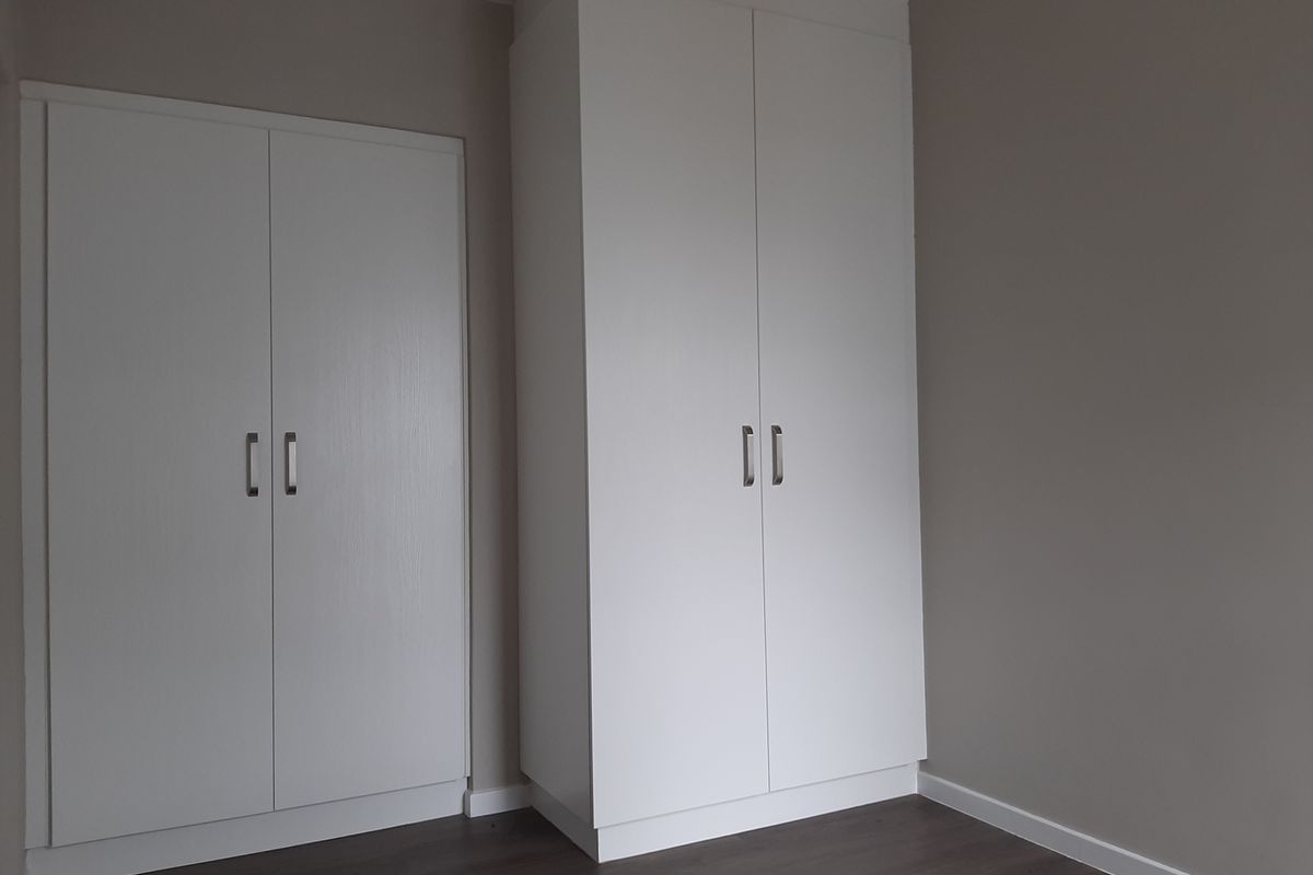 A clean, empty bedroom featuring modern white built-in cupboards and dark laminate flooring, providing a neutral canvas for personalization.